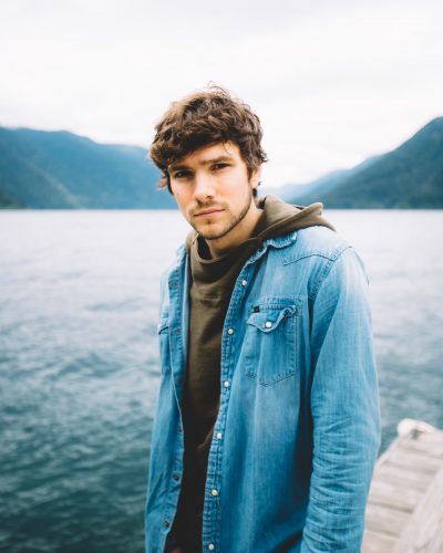 man in blue denim jacket standing near body of water during daytime