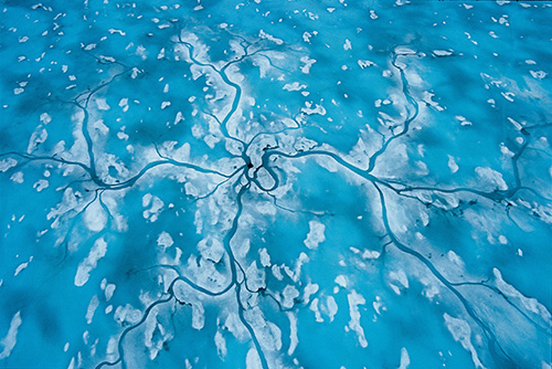 In the Arctic spring, meltwater channels drain toward and down a seal hole, returning to the sea.